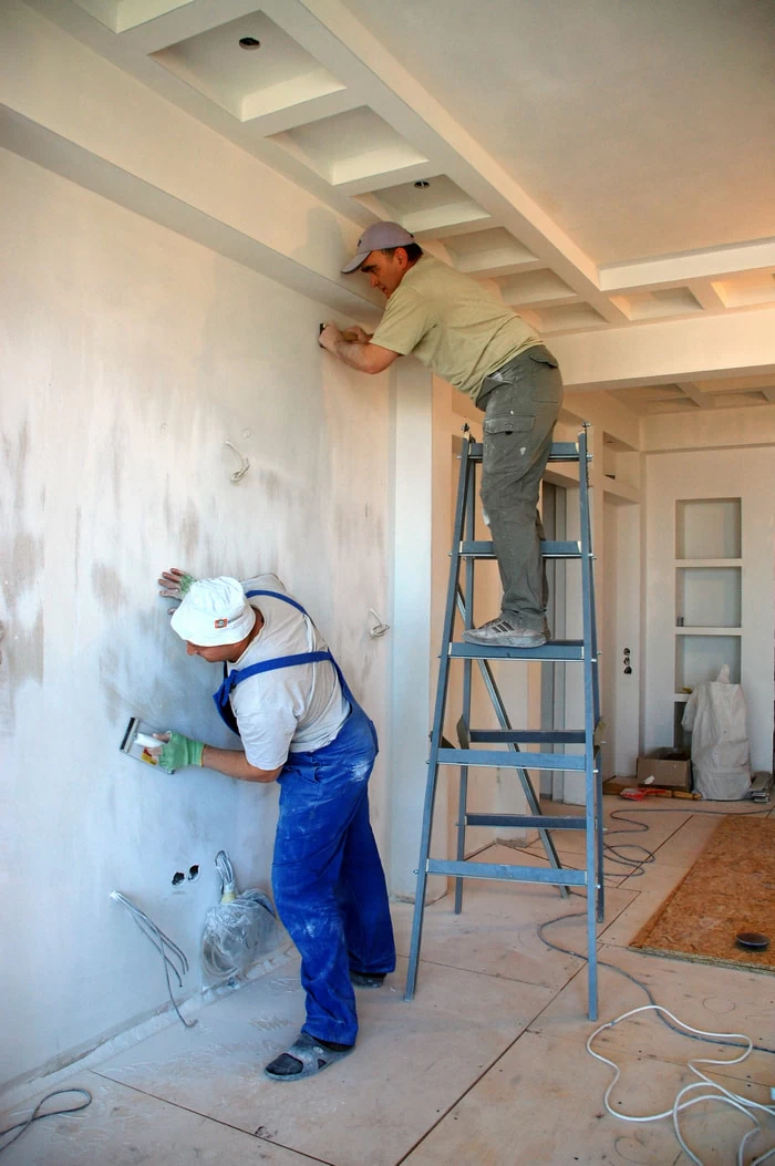 two men plastering a wall with one man on a ladder
